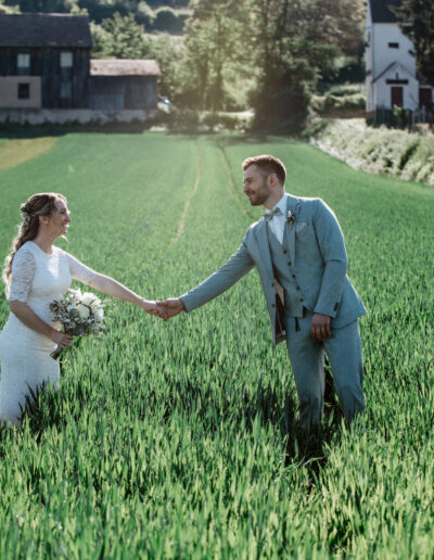 Braut und Bräutigam reichen sich die Hand in einem grünen Feld bei Lahr – natürliche Hochzeitsfotografie Lahr mit Persönlichkeit und ländlichem Charme.
