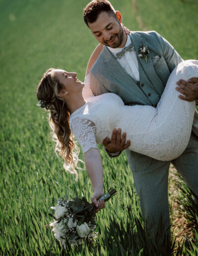 Fröhlicher Moment: Bräutigam trägt seine Braut auf einem Feld – Hochzeitsfotografie Lahr mit Persönlichkeit.