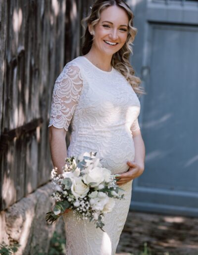 Lächelnde Braut im Spitzenkleid mit Blumenstrauß – natürliche Schwangerschafts- und Hochzeitsfotografie Lahr mit Persönlichkeit.
