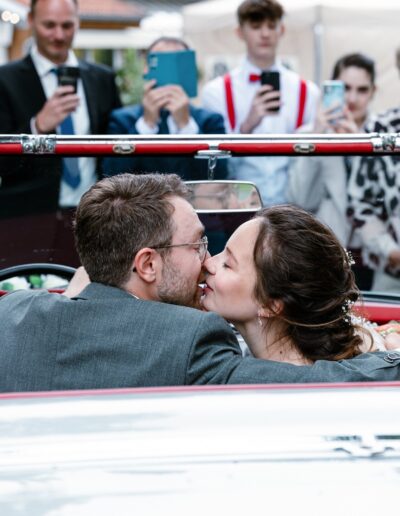 Das Brautpaar küsst sich im Cabrio, umgeben von jubelnden Gästen – lebendige Hochzeitsfotografie Lahr mit Persönlichkeit.