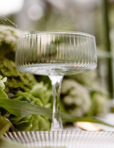 Stilvolle Tischdekoration mit einem eleganten Glas, umgeben von zarten Grüntönen – ein Blick für Details in der Hochzeitsfotografie von Helene Karsten.