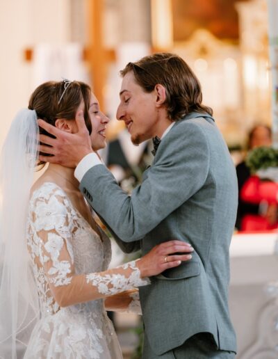 Ein liebevoller Kuss inmitten des festlichen Traualtars – ein klassisches Motiv der Hochzeitsfotografie, voller Emotionen und Intimität.