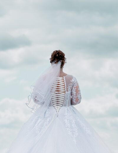 Mit dem Rücken zur Kamera und dem Himmel entgegen – ein kraftvoller Moment voller Eleganz und Anmut, eingefangen in kreativer Hochzeitsfotografie.