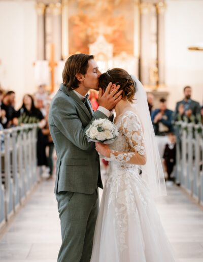 Ein emotionaler Kuss auf die Stirn der Braut nach der Trauung – das Brautpaar feiert seine Hochzeit in der Kirche mit einem innigen Moment voller Liebe und Dankbarkeit.