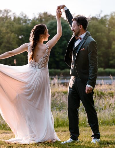 Ein Brautpaar tanzt auf einer Lichtung im Abendlicht – ihr luftiges Brautkleid fliegt im Kreis. Dieses Hochzeitsfoto fängt Leichtigkeit, Liebe und sommerliche Eleganz ein.