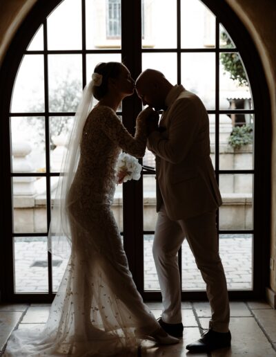 Ein zärtlicher Moment zwischen Braut und Bräutigam, der durch das Licht am Fenster in Szene gesetzt wird – ein ausdrucksstarkes Hochzeitsfoto voller Romantik und Stille.