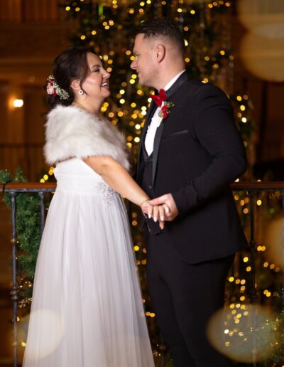Das Brautpaar lacht sich verliebt an, eingerahmt von festlicher Weihnachtsdeko – ein inniger Hochzeitsmoment mit Winterromantik und Lichterglanz.