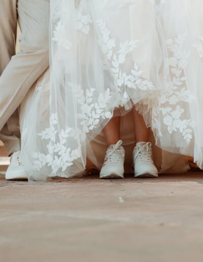 Unter dem wallenden Brautkleid blitzen sportliche, weiße Sneaker hervor, die sie gemeinsam mit dem Bräutigam trägt.