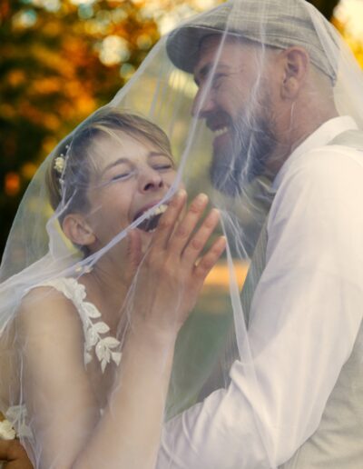 Braut und Bräutigam lachen ausgelassen unter dem Schleier, umgeben von goldenem Herbstlicht – ein spontaner und fröhlicher Hochzeitsmoment.