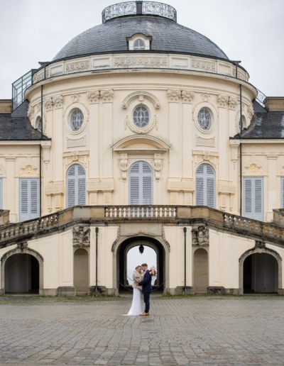 Ein Braupaar steht vor einem Schloss engumschlungen.