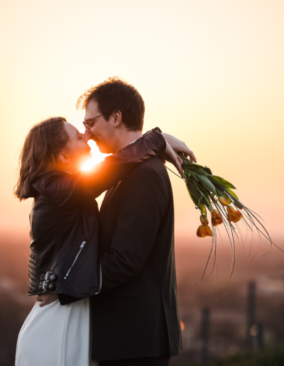 Sonnenuntergang, die Braut hat ihre Hände um den Nacken des Mannes gelegt, die Tulpen in ihren Händen liegen locker in ihrer Hand. neigen die Köpfe zueinander zum Kuss, die Sonne blitzt zwischen den zwei hindurch.