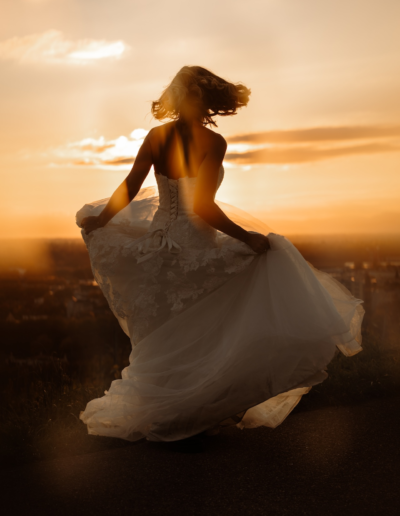 Sonnenuntergang, eine Braut dreht sich im Brautkleid schwungvoll im Kreis.