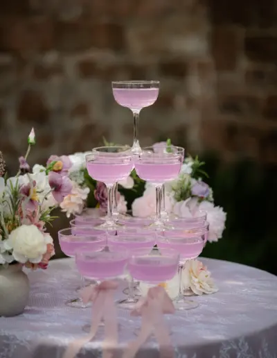 Cocktailglas Pyramide auf einem runden Tisch der mit Blumen drapiert ist. In den Gläsern befindet sich eine rosafarbene Flüssigkeit.