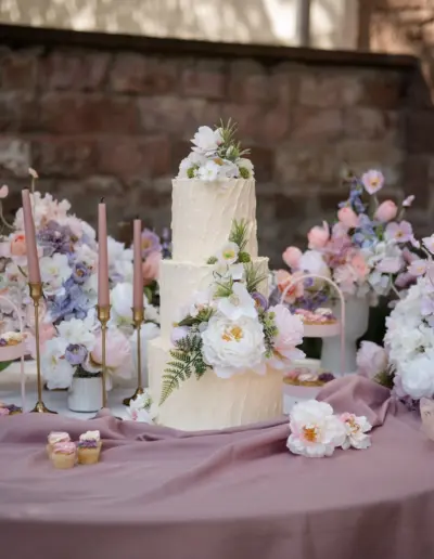 Ein dekorierter Tisch mit Hochzeitstorte. Ganz viele pastellfarbene Blumen drum herum.